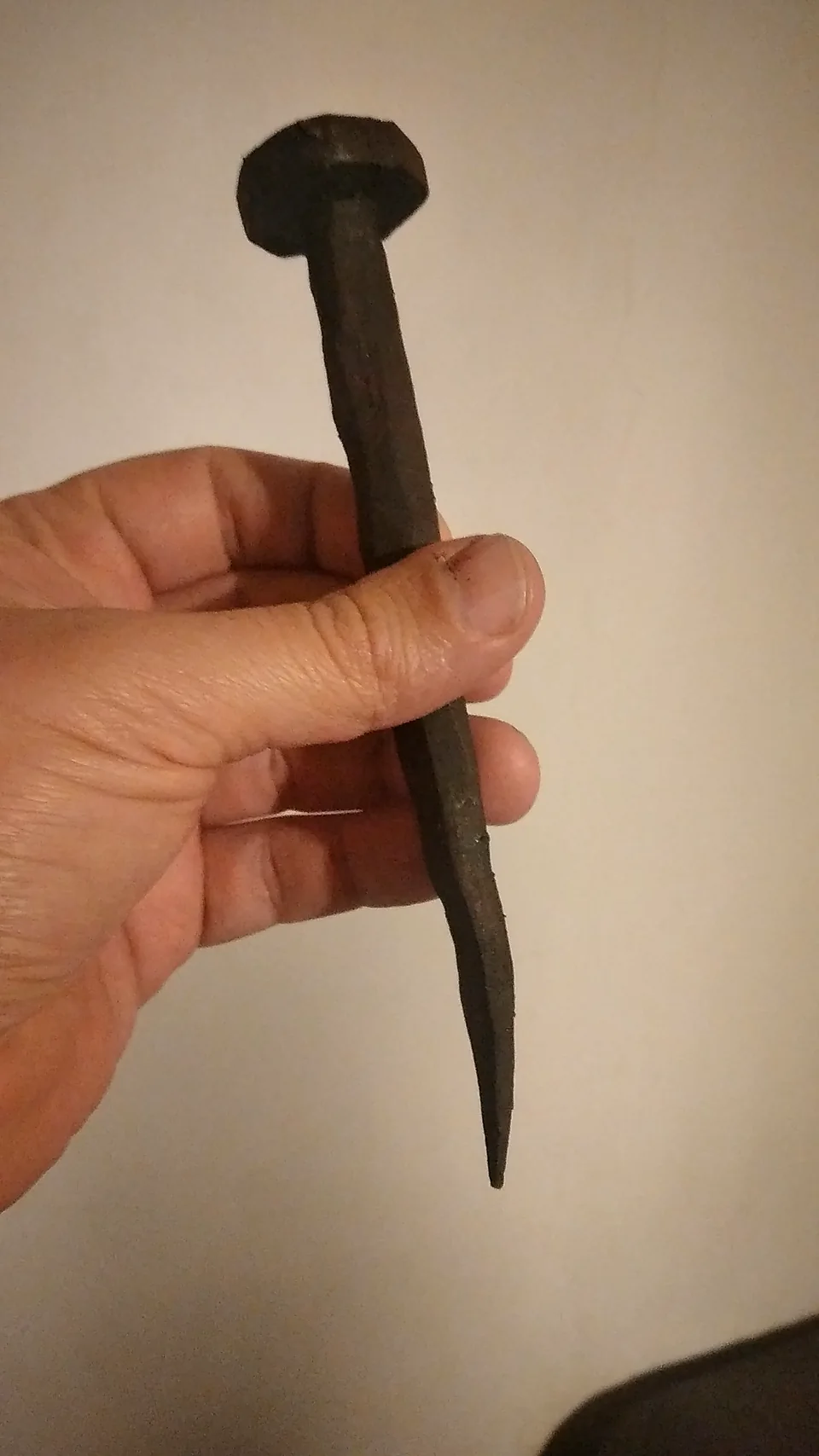 Mano che regge la riproduzione di un chiodo romano forgiato, oggetto di scena